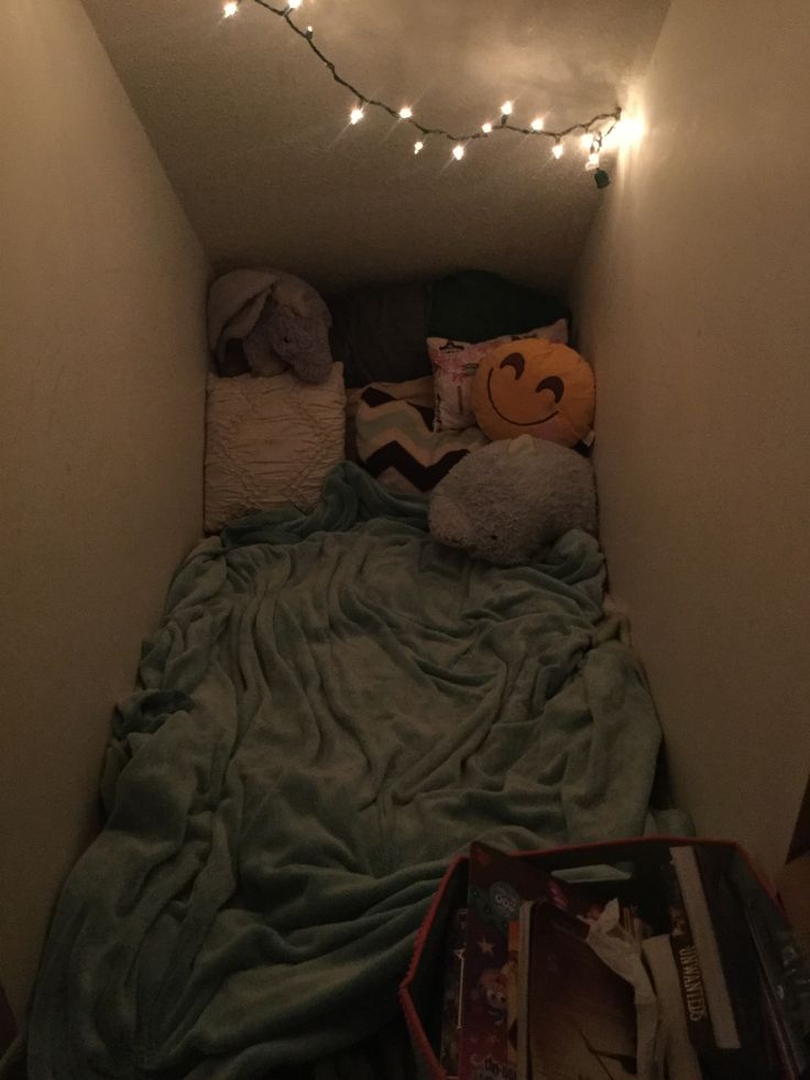 a bed with blankets, pillows and lights in a small room filled with stuff on the floor