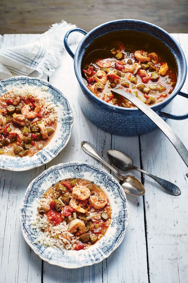 two plates with shrimp and rice on them next to a pot full of stew, spoons and utensils