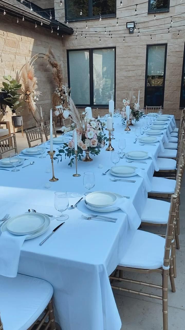 a long table is set with white plates and silverware for an outdoor wedding reception