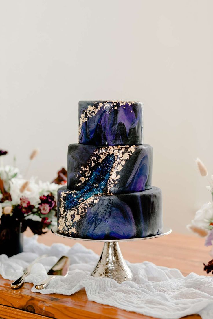 a three tiered cake with blue and purple marbled icing sitting on top of a wooden table