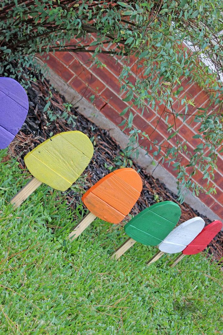 four wooden paddles sitting in the grass near a brick wall