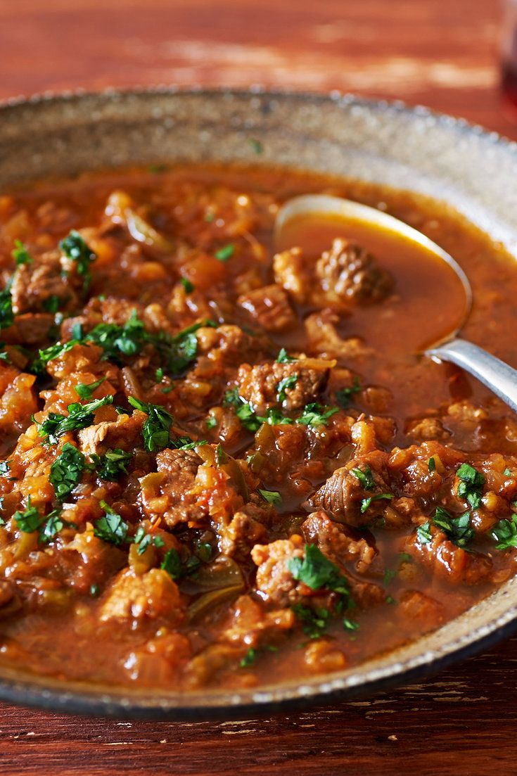 a bowl filled with meat and vegetables on top of a wooden table next to a spoon