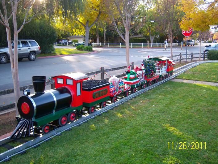 a toy train is on the tracks in front of a street and cars parked along side it