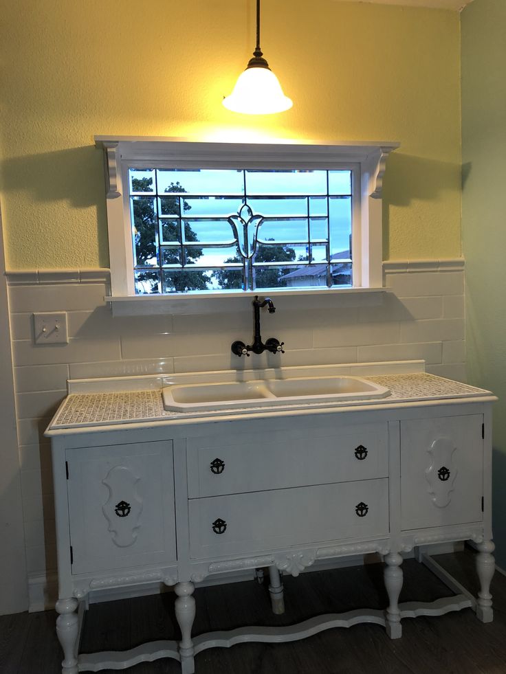 a white sink sitting under a window next to a counter top with two faucets