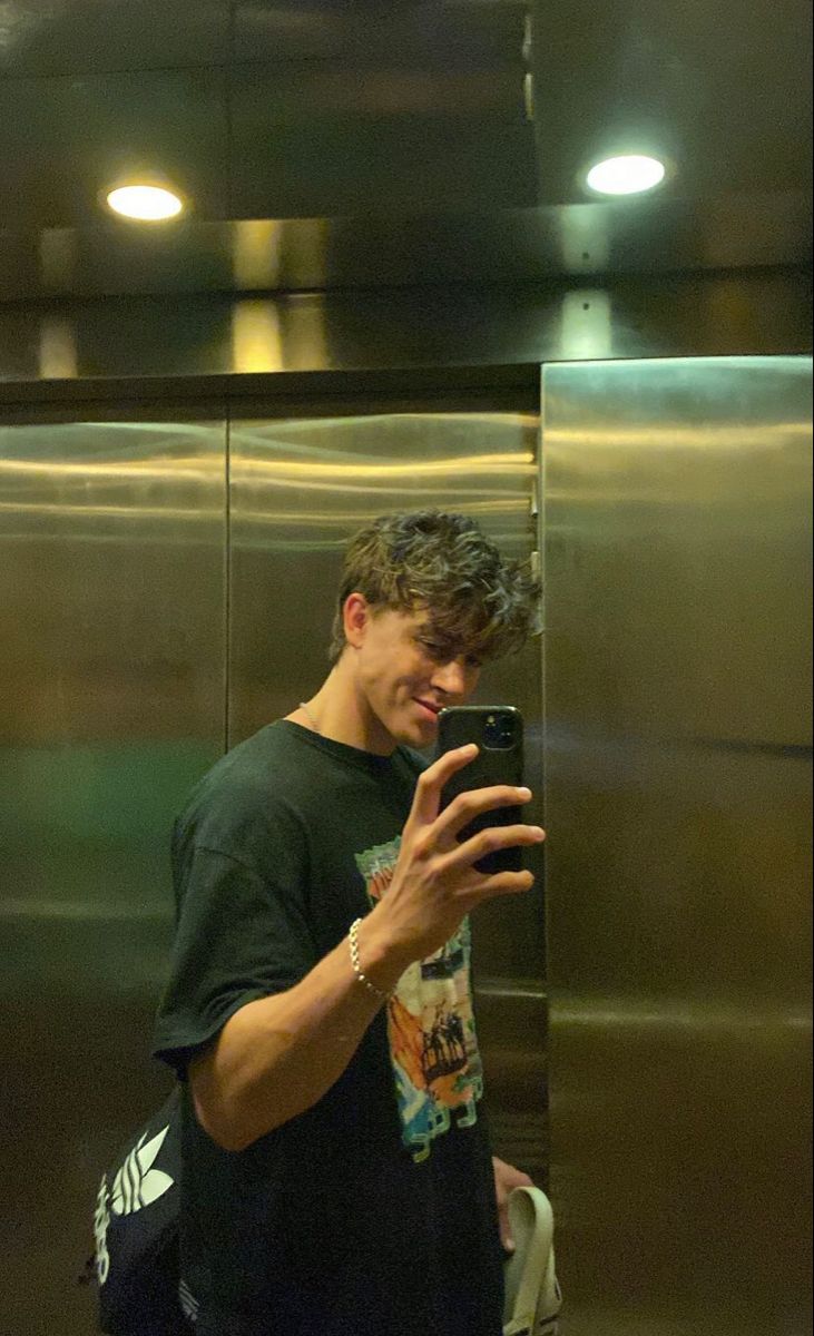 a young man taking a selfie in front of an elevator with his cell phone