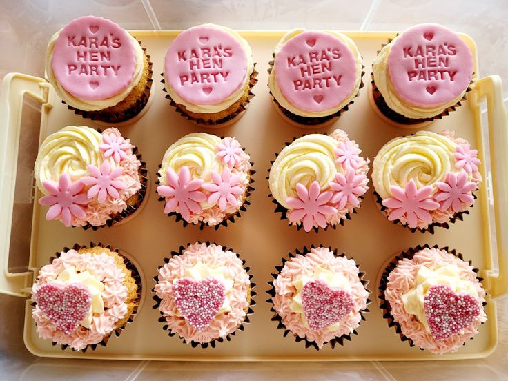 cupcakes decorated with pink frosting and hearts are arranged in a tray on the table