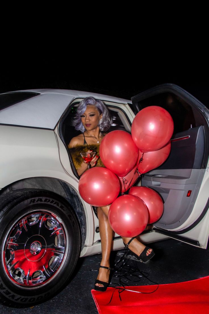 a woman is sitting in the back of a car with red balloons attached to it