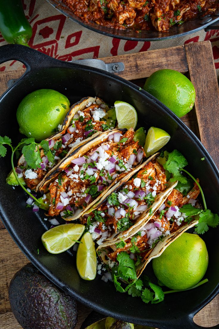 three tacos in a skillet with limes and cilantro