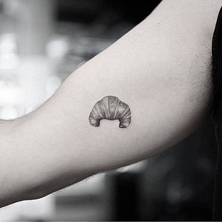 a black and white photo of a person's arm with a small croissant tattoo on it