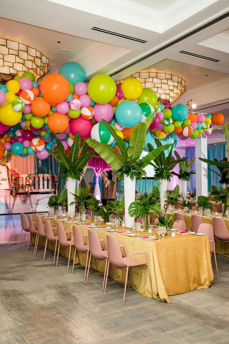 a room filled with lots of tables covered in balloons and greenery on top of them