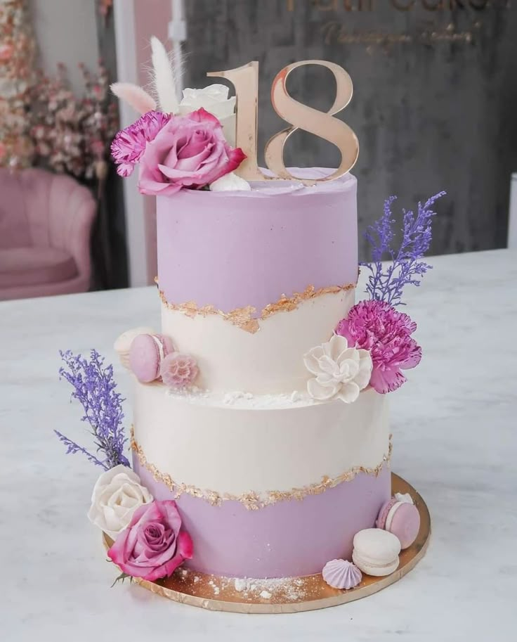 a three tiered cake with pink flowers and feathers on the top is decorated in gold