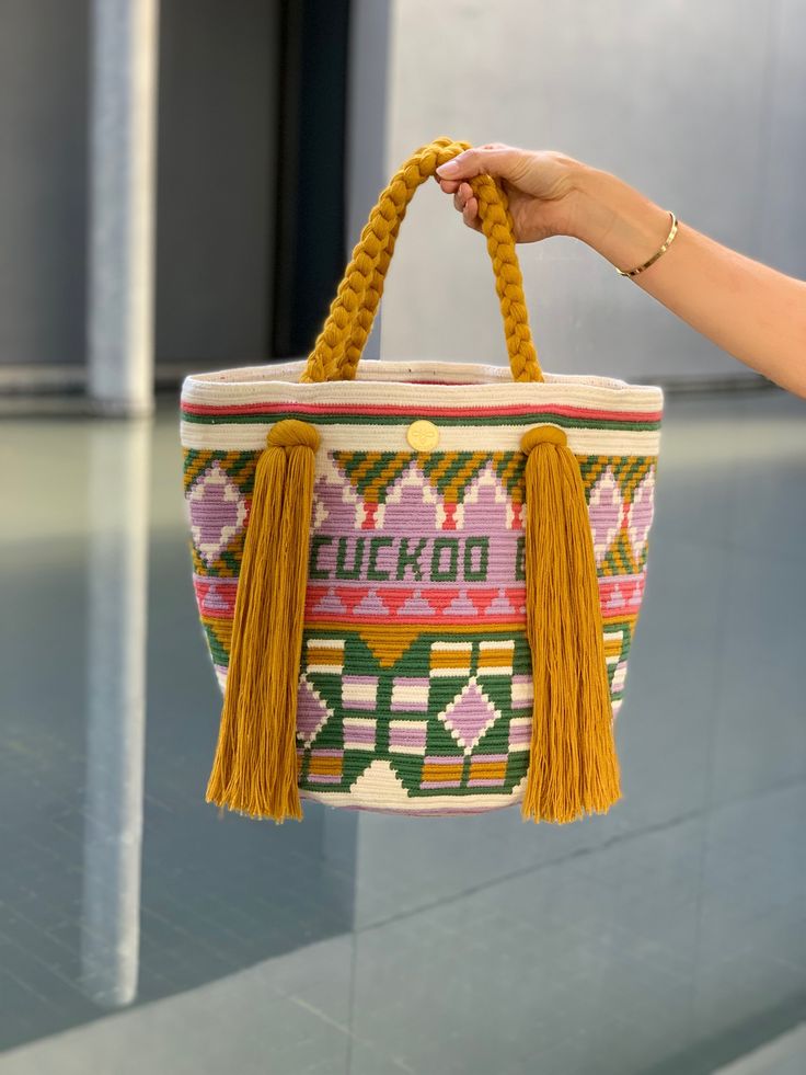 The Maria tote bag, is traditionally called Mochila by the Wayúu, the Colombian indigenous group on the Caribbean Coast, that hand-wove them. This detailed colorful bag can take up to 3 weeks to be made by crochet with a single cotton thread, by Wayuu women in La Guajira. The oversized bucket-shaped body of the bag feature woven traditional patterns which tell stories of the tribe's daily life. The short braided handles are finished with extra long tassels and are perfect to carry under the arm Bohemian Bucket Bag With Braided Top Handle, Artisan Woven Bucket Bag, Artisan Handwoven Bucket Bag, Market Tote Bucket Bag With Braided Handles, Weaved Bucket Bag, Bohemian Top Handle Bucket Bag For Daily Use, Bohemian Woven Bucket Shoulder Bag, Handwoven Tote Bucket Bag, Bohemian Woven Bucket Shape Shoulder Bag