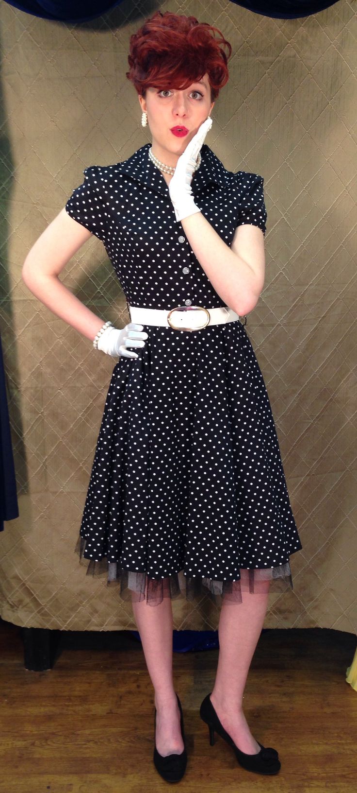 a woman in a polka dot dress and white gloves poses for the camera with her hands on her hips