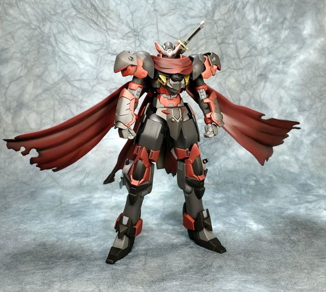 a robot that is standing up on a gray surface with a red cape around it's neck