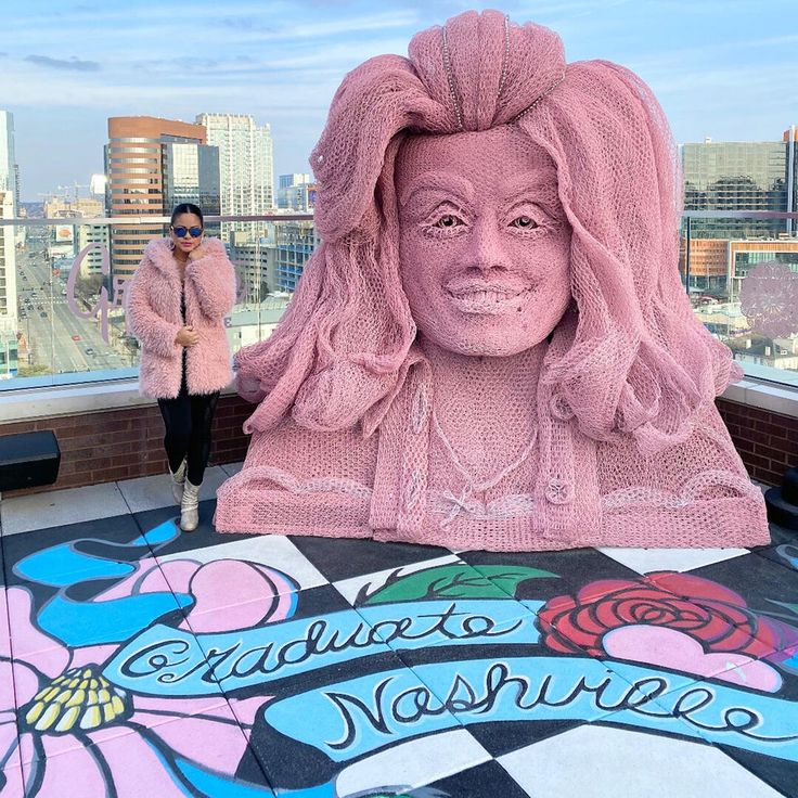 two women standing in front of a large pink statue on top of a tall building