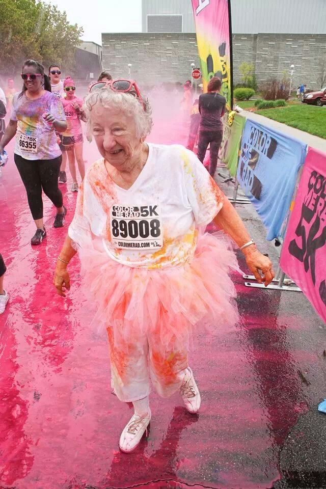 an older woman running in the color run with pink and orange powder on her face