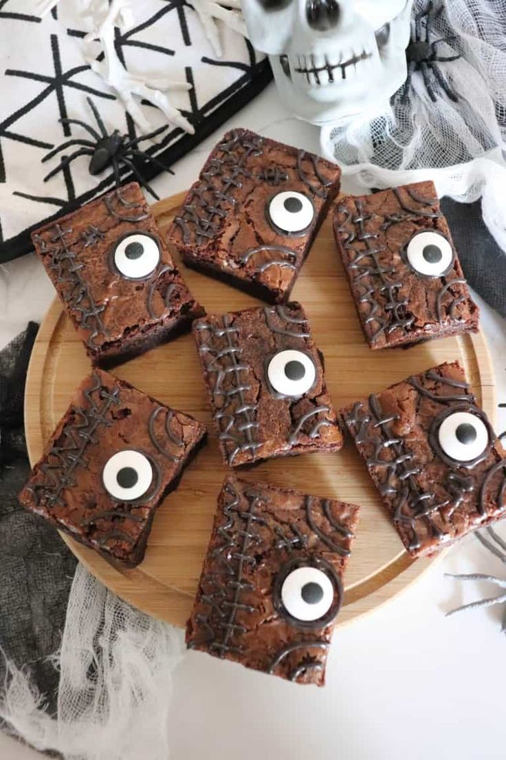 chocolate brownies with googly eyes on a wooden plate next to halloween decorations and skulls