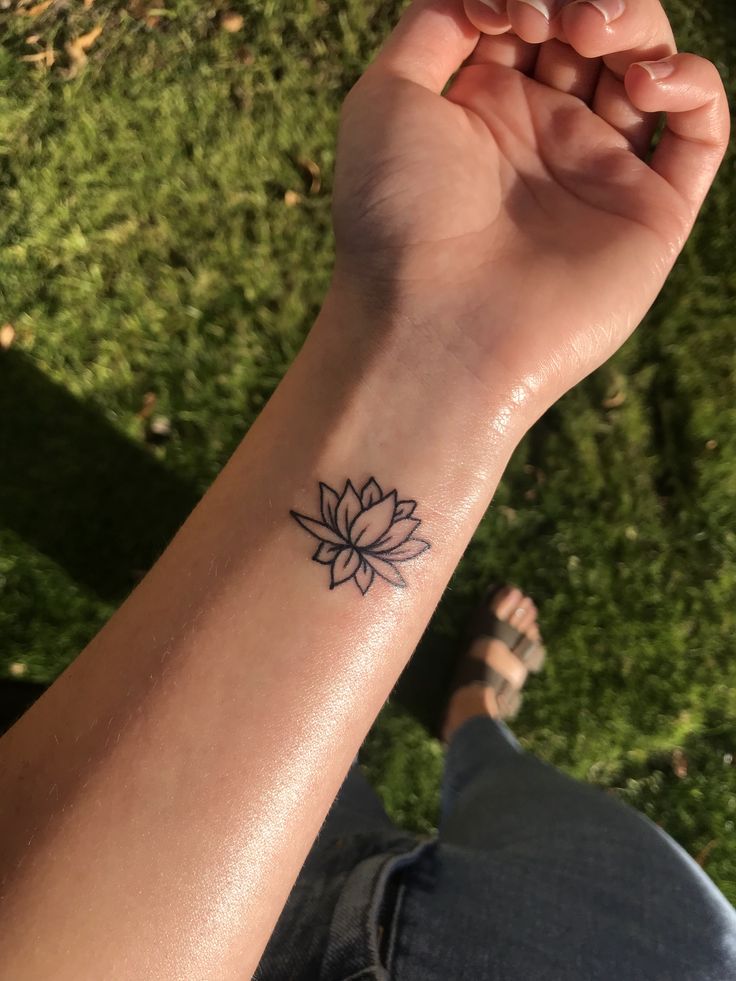 a woman's arm with a small lotus tattoo on the left side of her wrist