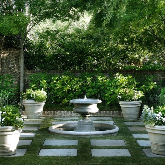 an outdoor garden with potted plants and water fountain in the center, surrounded by stone pavers