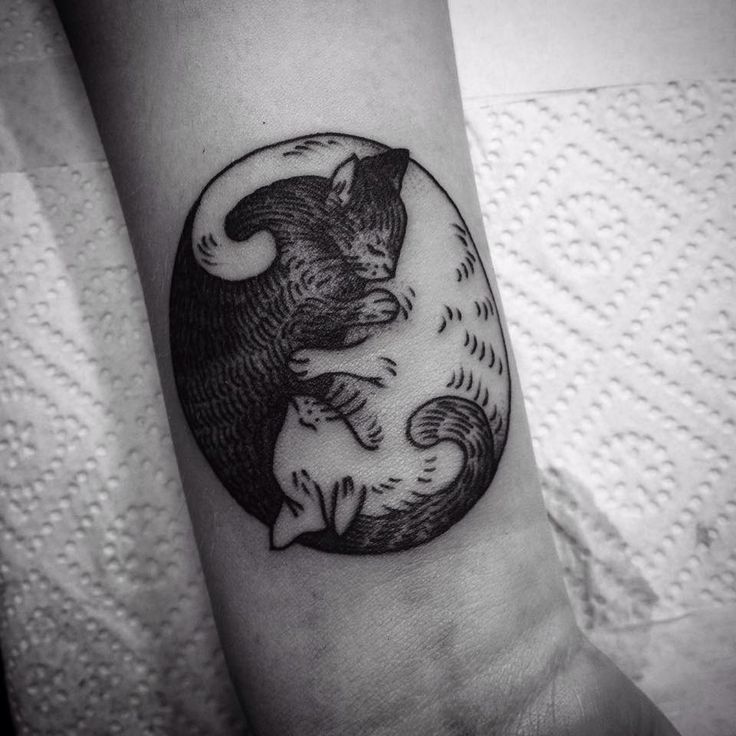 a black and white photo of a cat in a circle tattoo on the left arm