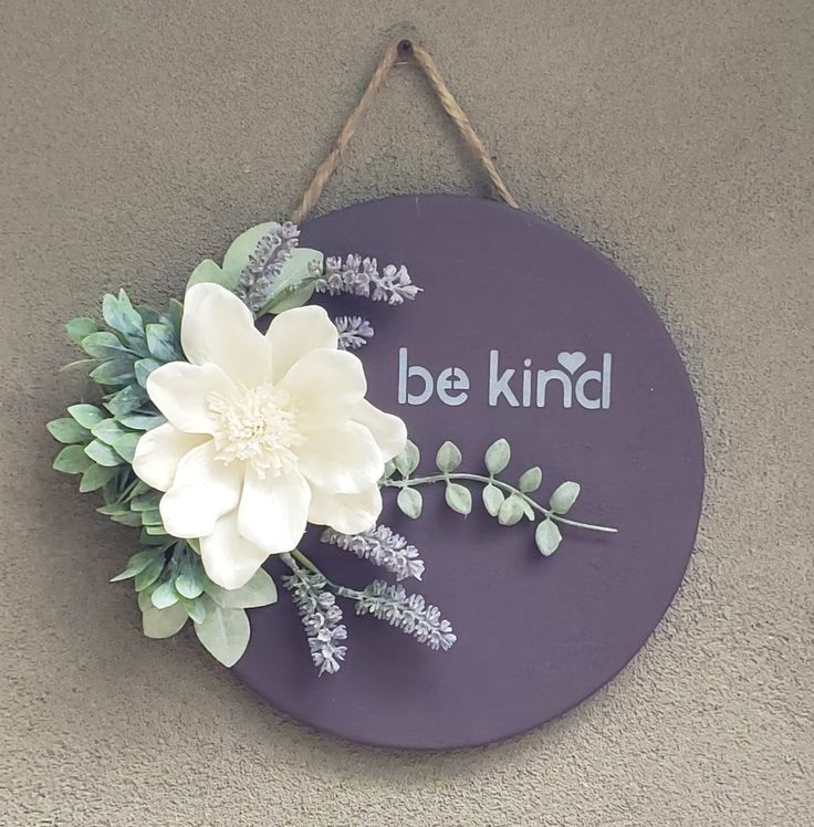 a sign that says be kind with flowers and leaves hanging from the side of it