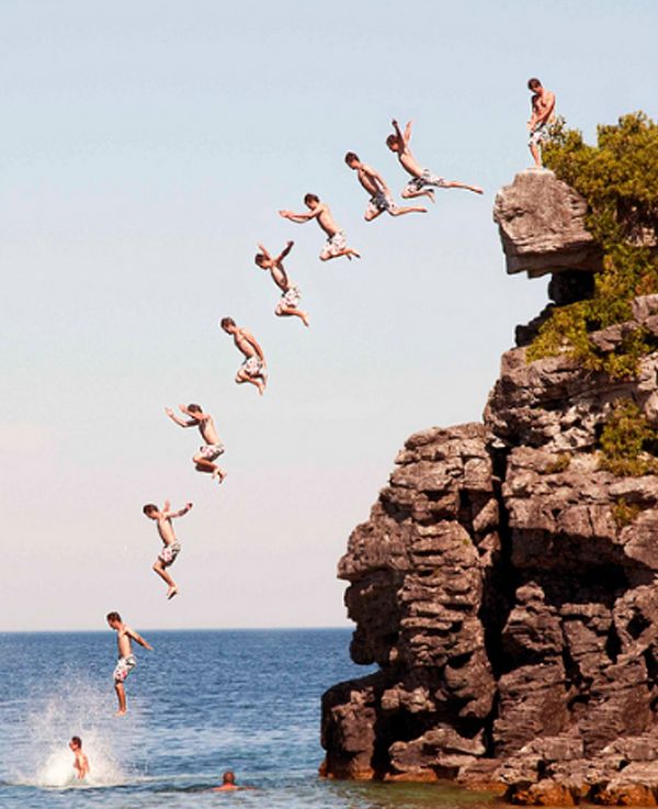 several people jumping off rocks into the water from a cliff in front of an ocean