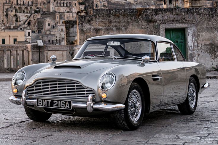 an old silver car parked in front of a building on a cobblestone street