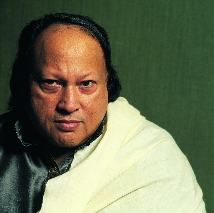 a man in a black leather jacket and white shawl looking at the camera with an angry look on his face