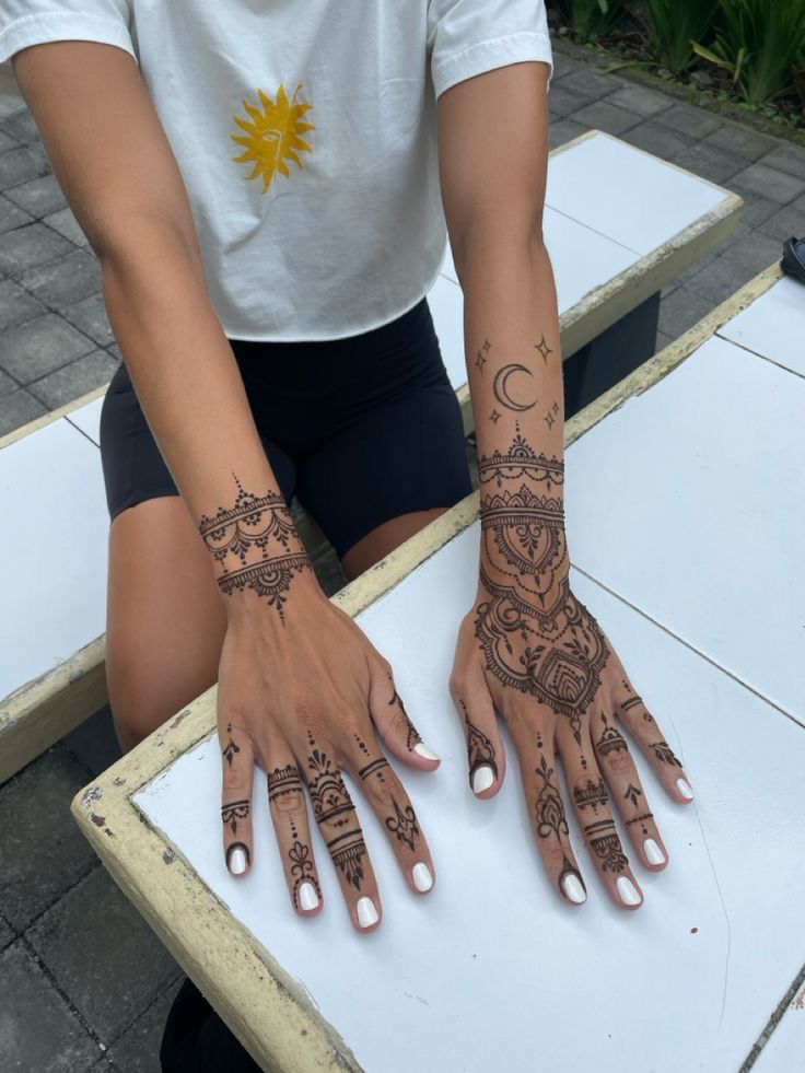 a person with henna tattoos on their hands sitting at a white table outside in front of some plants