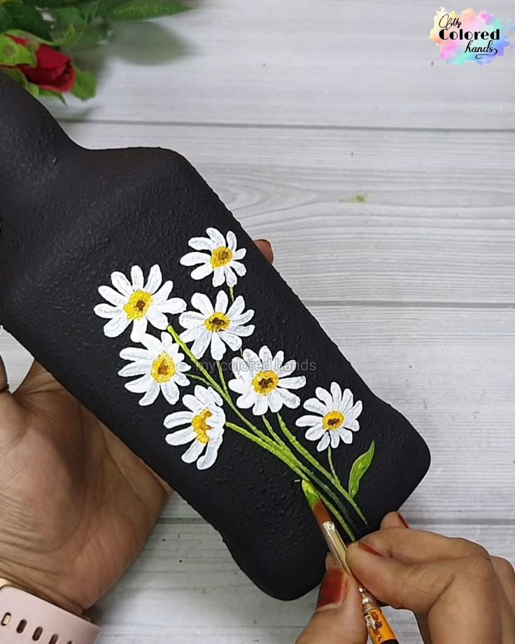 someone is painting daisies on the back of a black leather case with white and yellow flowers