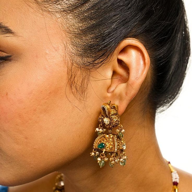 Introducing the Neema Moissanite Mor Jhumkas by Yamoona--a perfect match to the Nakashi Short Necklace. These jhumkas showcase the same exquisite antique gold-plated design with intricate peacock detailing, moissanites, and emerald bead hanging stones. Elevate your style with these opulent jhumkas, capturing timeless elegance and heritage in gold plated workmanship. 22k Gold Chandbali Jhumkas With Cutdana, 22k Gold Chandbali Jhumkas With Tilla, 22k Gold Chandbali Jhumkas For Festive Occasions, 22k Gold Chandbalis For Wedding And Navratri, Ceremonial Chandbali Jhumkas With Intricate Design, Yellow Gold Kundan Jhumkas With Latkans, 22k Gold Meenakari Chandbali Jhumkas, 22k Gold Bollywood Chandbali Jhumkas, 22k Gold Chandbalis With Latkans Temple Jewelry