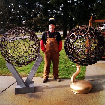 a man standing next to two metal balls