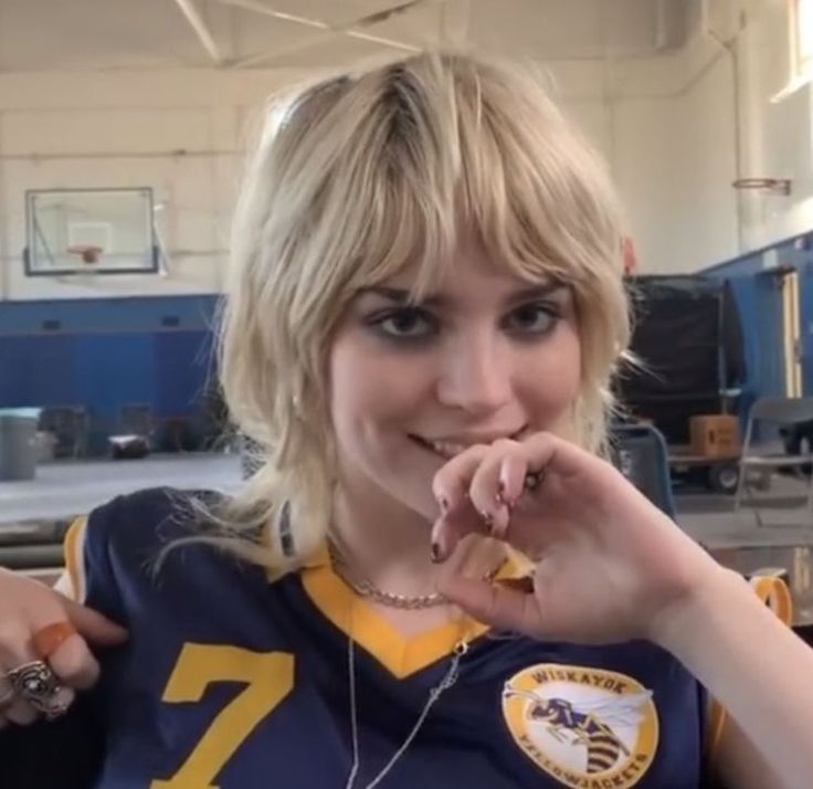 a woman with blonde hair wearing a football uniform and holding something in her hand while posing for the camera