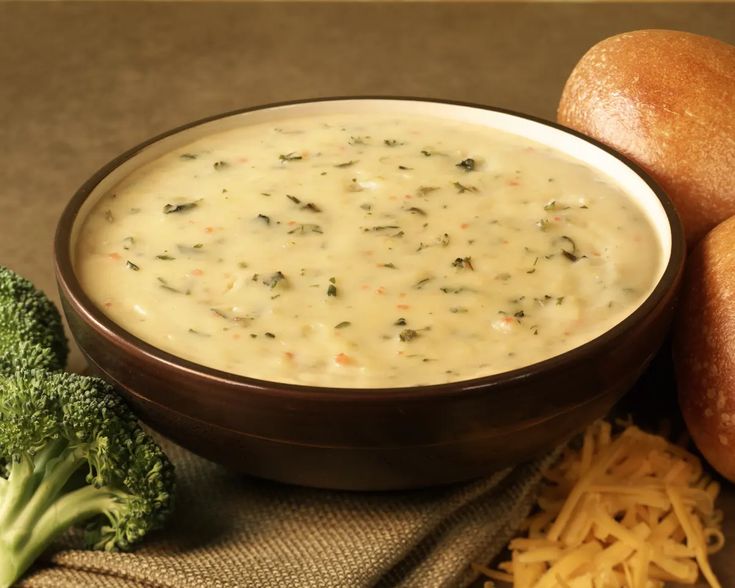 broccoli and cheese dip in a brown bowl next to bread on a cloth