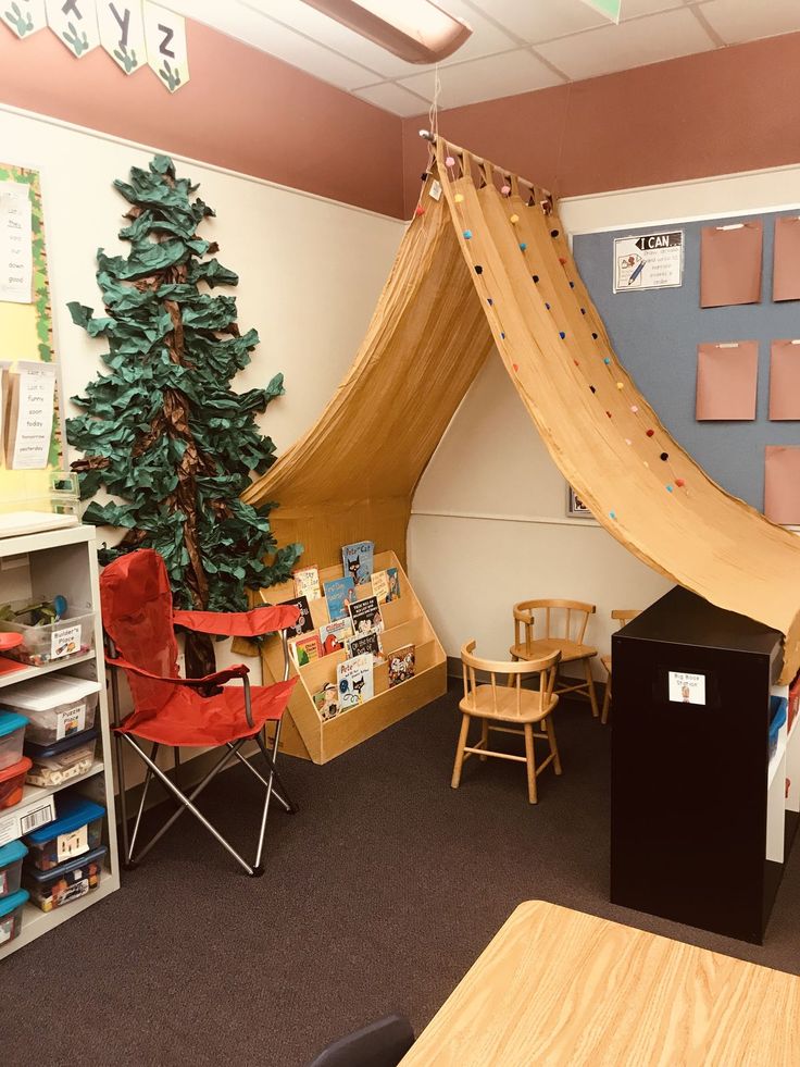 a room with a tent, desks and chairs next to a small christmas tree