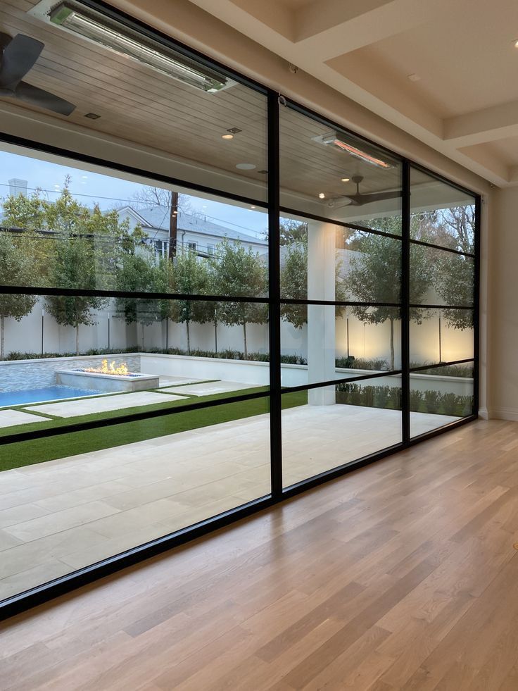 an empty room with large glass windows overlooking a backyard and pool area in the background