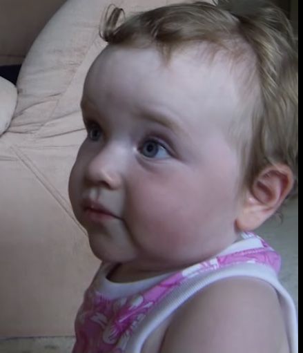 a baby girl with blue eyes and blonde hair wearing a pink dress looking at the camera