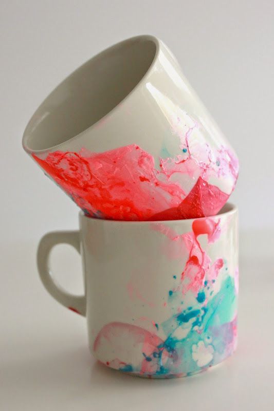 two coffee mugs with different colored paint splattered on the cups side by side