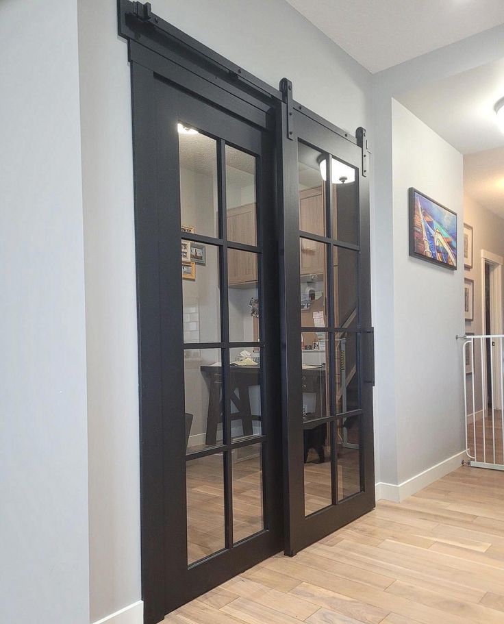 an empty room with black doors and wood flooring in front of a white wall