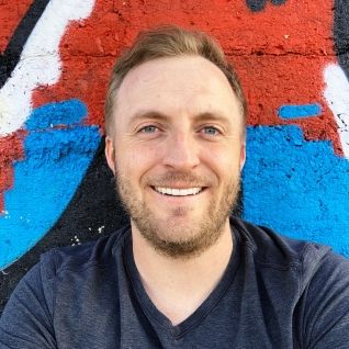 a man is smiling in front of a colorful wall