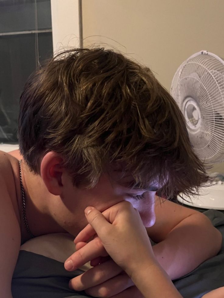 a young man laying in bed next to a fan