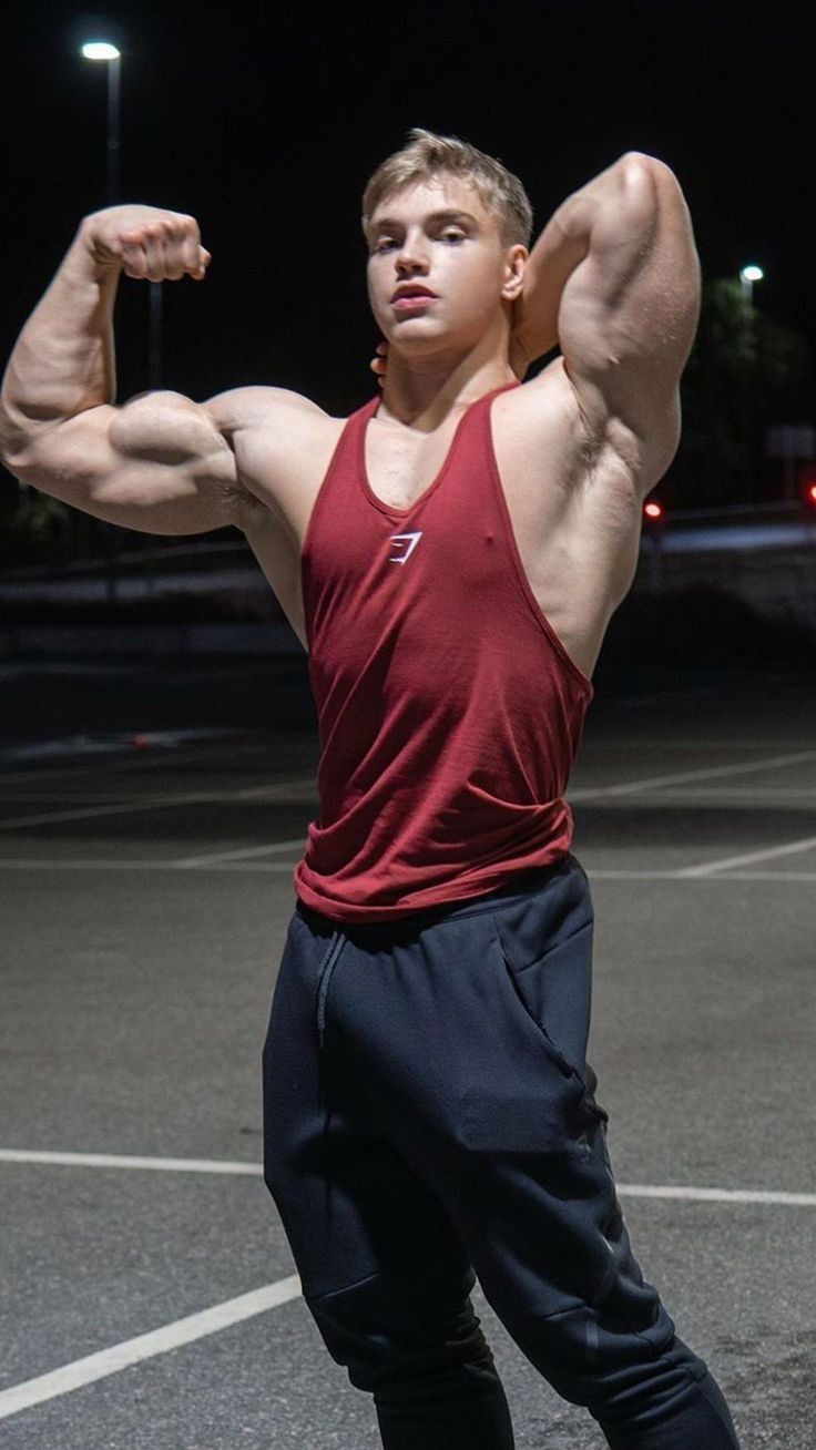 a young man flexing his muscles in the parking lot at night with no one around him