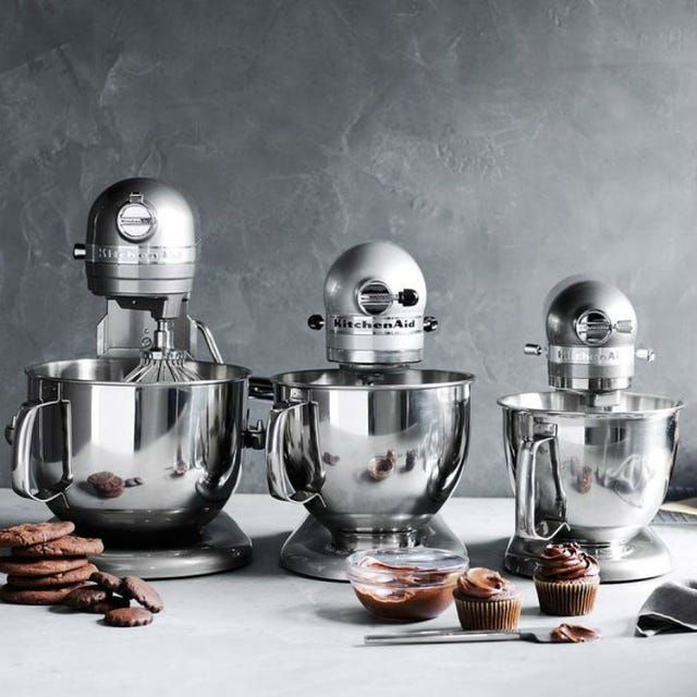 three silver mixers sitting on top of a counter next to cookies and doughnuts