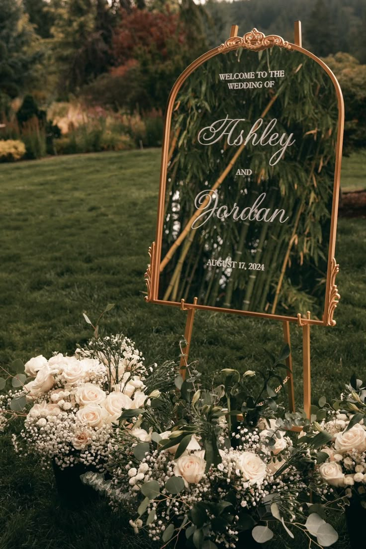 a wedding sign with flowers and greenery on the grass in front of a field