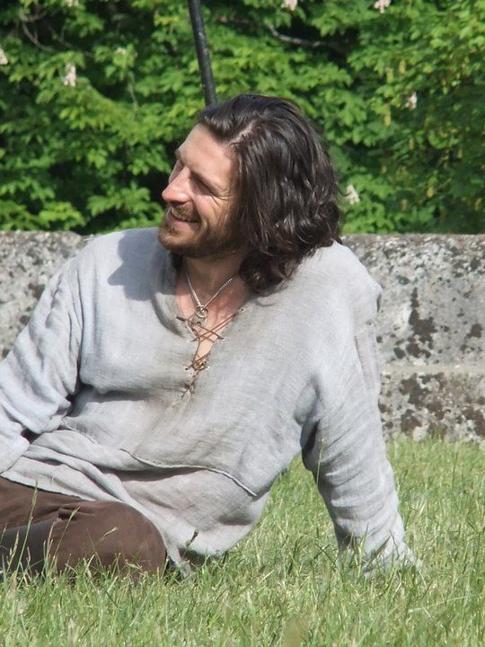 a man with long hair sitting in the grass and looking off to the side,