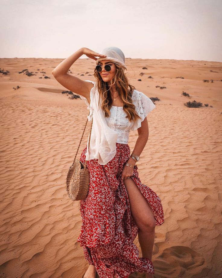 a woman standing in the sand with her hand on her head and wearing a hat