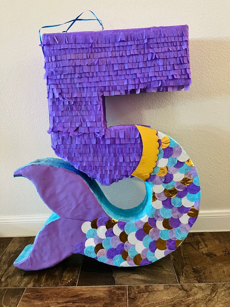 the letter e is made out of purple paper and has fish on it's tail