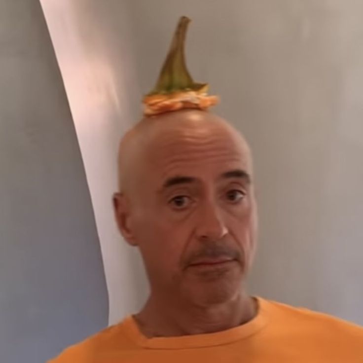 a bald man wearing an orange shirt with a gold crown on top of his head