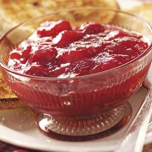 a glass bowl filled with cranberry sauce on top of a plate next to bread