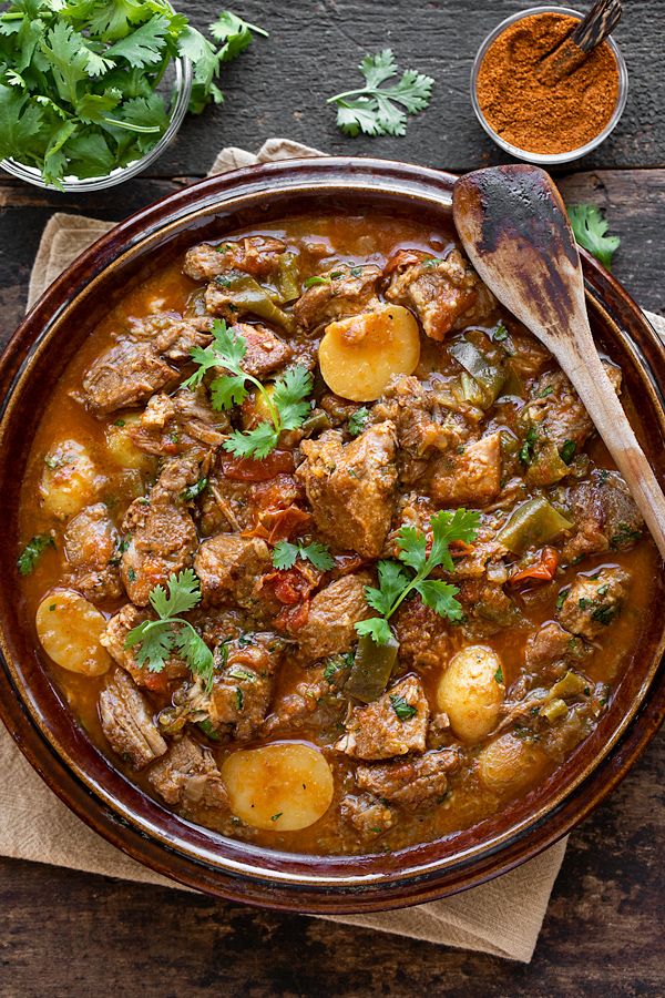 a bowl filled with meat and potatoes on top of a wooden table next to spices